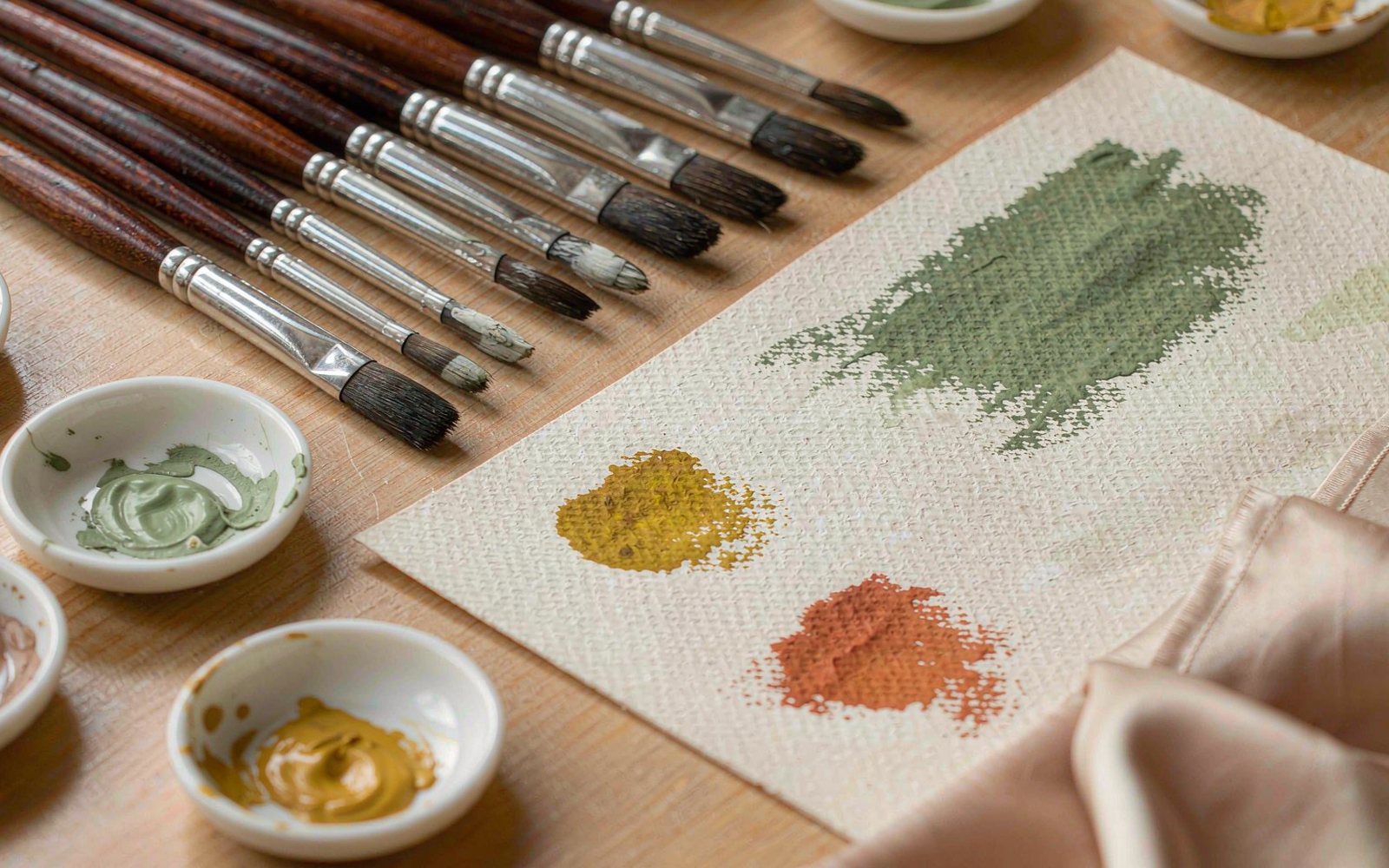 Studio flat lay of paintbrushes, pigments and a colour card with silk swatches